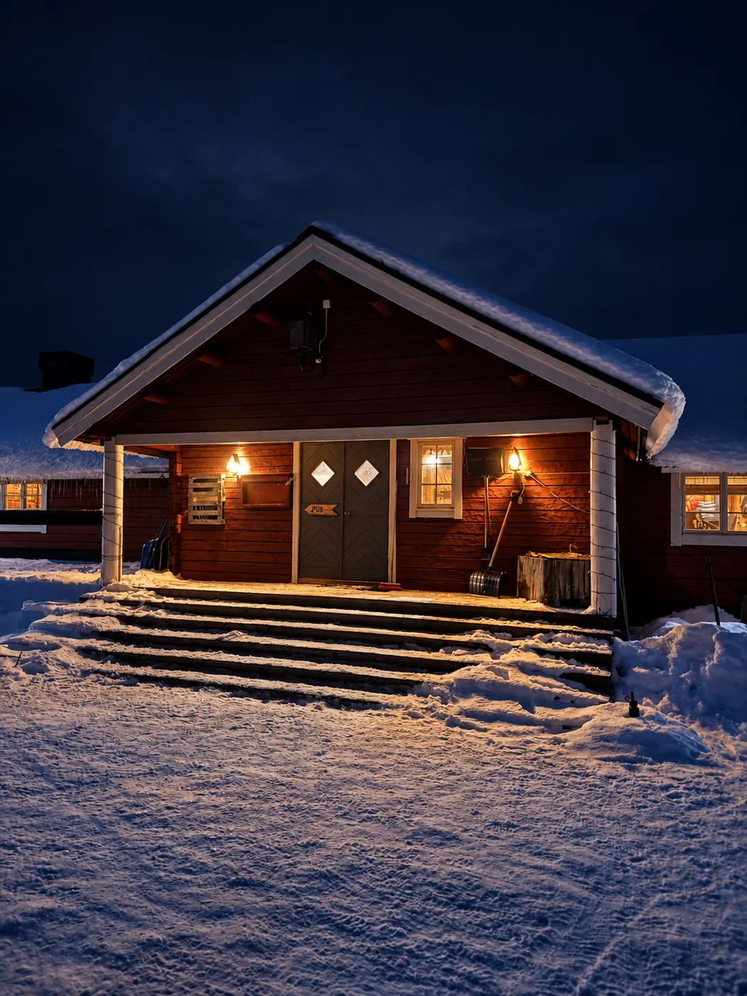 Entrén till Vargen en vinterkväll, lamporna tända och snö på trappan